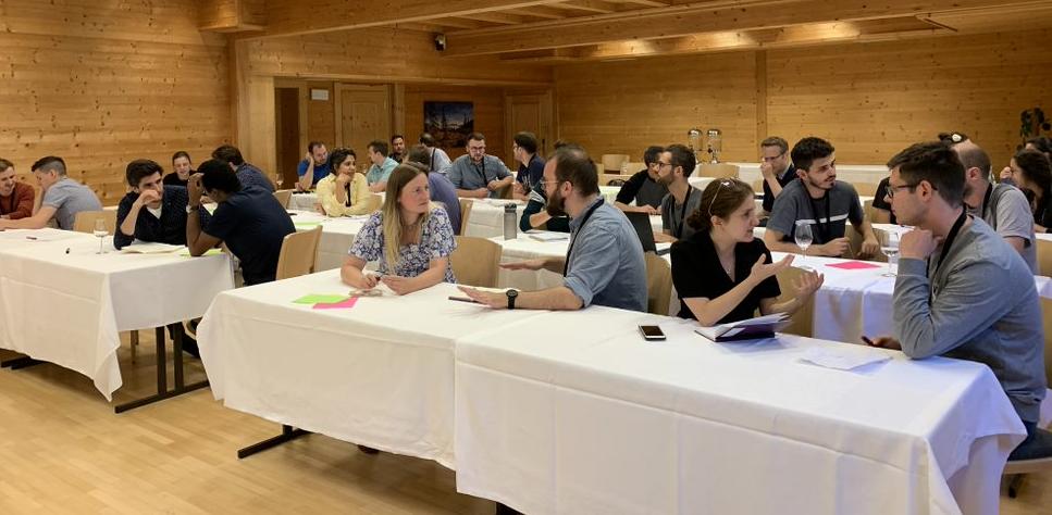 Attendees of the CuPiD inaugural meeting in Alpbach (September 2022) have one-to-one break out conversations. They are sat at tables, in a wooden room. 